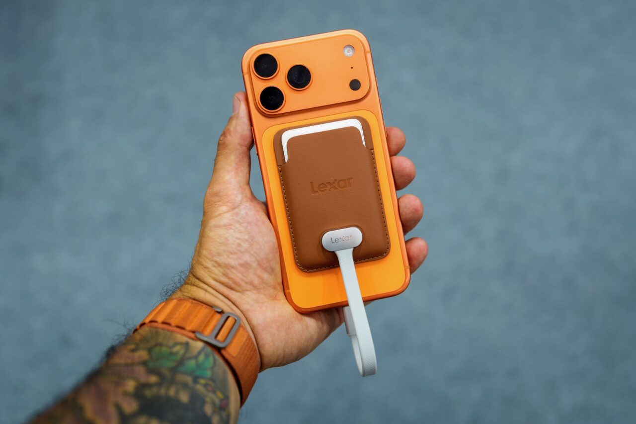 Lexar Muse SSD fin monde iPhone SSD Lexar Muse dans son étui marron aimanté au dos d'un iPhone orange, avec son câble blanc.