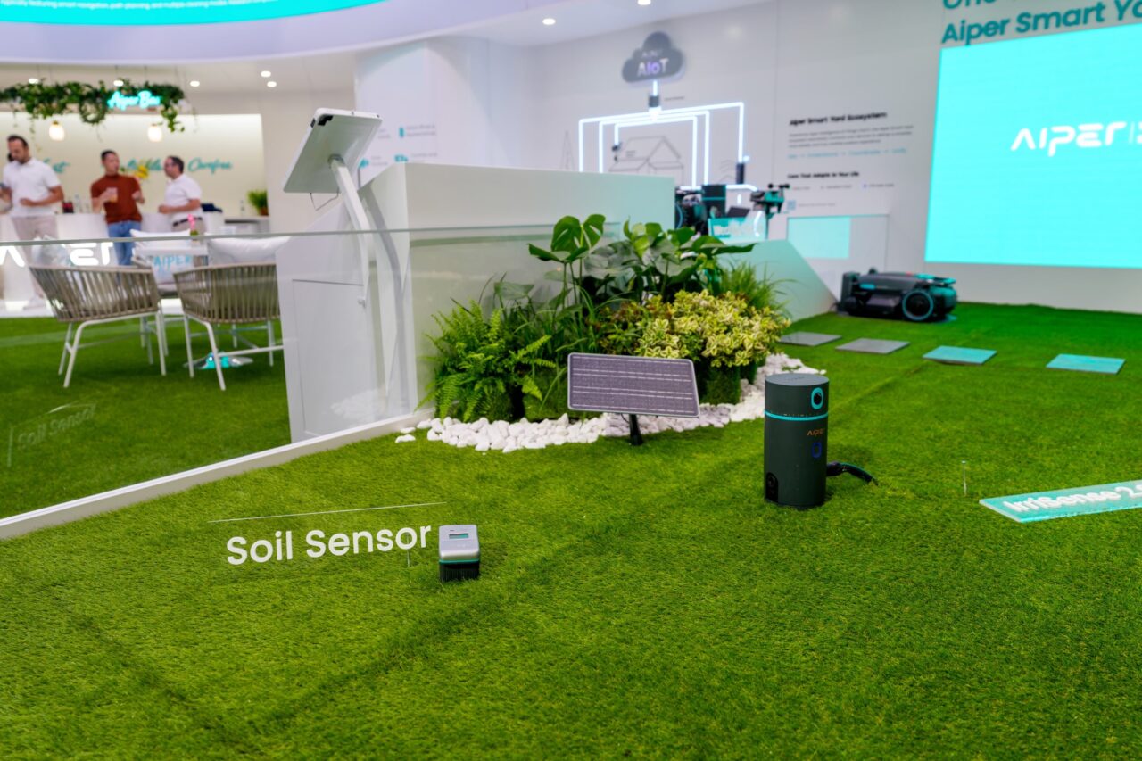 aiper soil sensor Capteur de sol Aiper Soil Sensor posé sur une pelouse de démonstration, avec un petit panneau solaire à l'arrière.