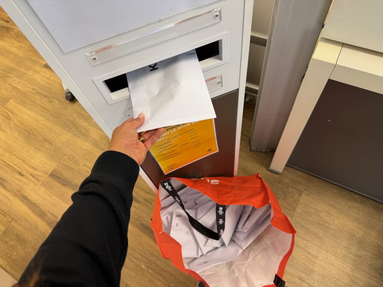 Une enveloppe de flammes LOKAN est glissée dans la boîte aux lettres de La Poste, à côté du sac rempli de commandes.
