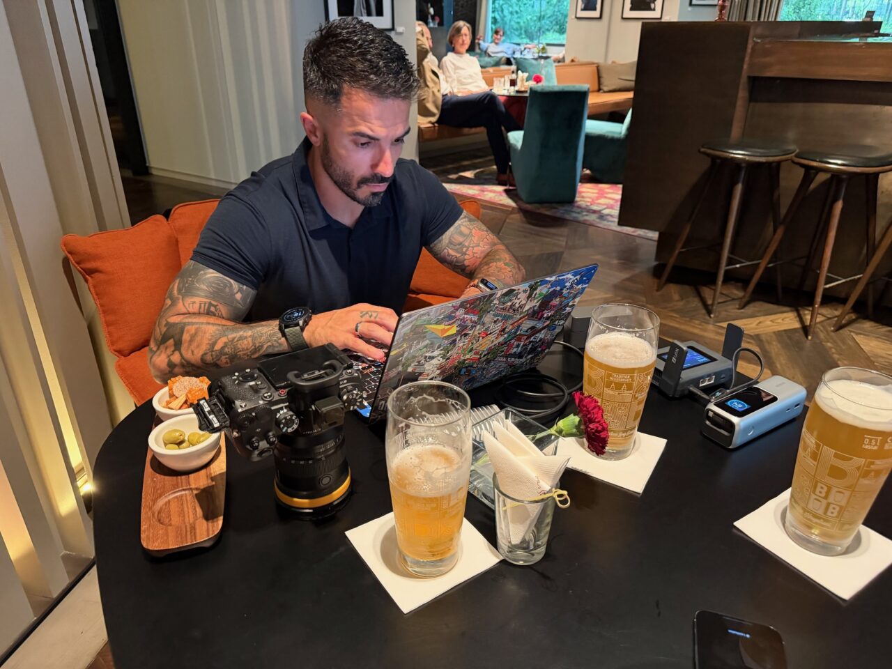 lokan aperitif montage macbook slate 7 pro LoKan travaille sur son MacBook à une table avec son appareil photo, un routeur Slate 7 Pro et des verres de bière.