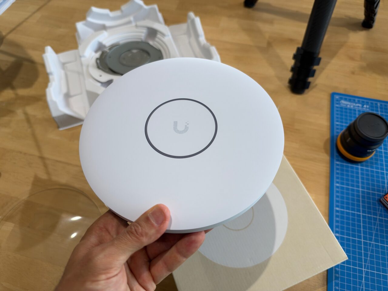 Borne UniFi U7 Pro XGS blanche tenue en main, devant son emballage et son support de fixation.